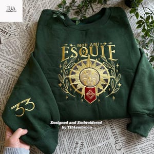 Puede incluir: Sudadera verde oscuro con bordado dorado. El diseño incluye el texto "MON AMI ESQUIE" sobre un emblema de sol y el número "33" en la manga. Diseñado y bordado por THAembroco.
