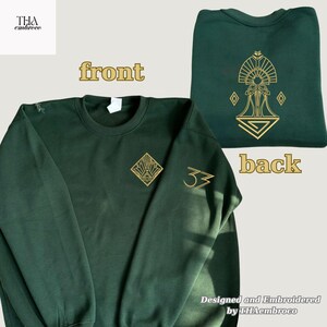 Puede incluir: Sudadera verde oscuro con bordado dorado. La parte delantera presenta un diseño geométrico y el número 33. La parte trasera muestra un diseño dorado detallado. El texto "THA embroco" está en la esquina superior izquierda.