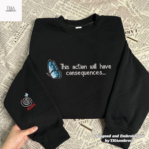 Puede incluir: Sudadera negra con una mariposa azul y el texto "This action will have consequences...". La manga izquierda presenta un diseño "Rewind". La sudadera está diseñada y bordada por THAembroco.