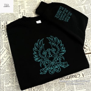 May include: Black sweatshirt with a teal phoenix emblem. The sleeve has the text "IN WAR, VICTORY. IN PEACE, VIGILANCE. IN DEATH, SACRIFICE." Designed and embroidered by Thaembroco.