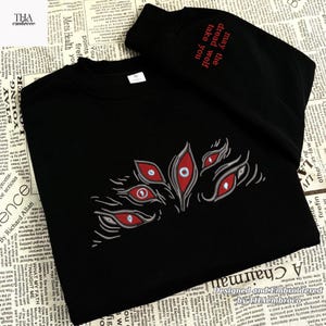 May include: Black sweatshirt with an embroidered design of multiple red and white eyes. The text "may the dread wolf take you" is embroidered on the sleeve. The sweatshirt is a crew neck style.
