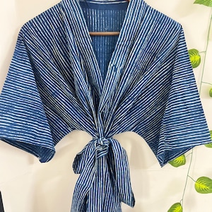 May include: A blue and white striped robe hanging on a wooden hanger. The robe is tied at the waist with a matching belt. The fabric has a textured appearance, and the stripes are vertical.