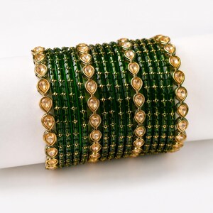 May include: A set of dark green glass bangles featuring a textured surface with small gold-coloured beads and teardrop-shaped clear stones arranged in a vertical line pattern along the outer edge of the circular wrist jewellery pieces.