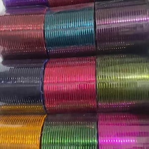 May include: A collection of thin, metallic bangles arranged in a grid of twelve distinct colour sets. Each set consists of multiple stacked rings with a shiny, reflective finish in shades of purple, red, black, teal, magenta, lime green, and gold.