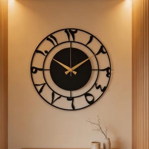 Könnte beinhalten: Eine große, runde Wanduhr mit einem schwarzen Metallrahmen und indo-arabischen Ziffern. Die Uhr hat ein massives schwarzes Zifferblatt in der Mitte sowie dünne, goldfarbene Stunden- und Minutenzeiger. Das Design ist offen gestaltet.