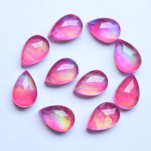 May include: Ten teardrop-shaped cabochons with a faceted top surface. Each piece displays a translucent pink hue with iridescent, glowing yellow and orange internal color shifts that create a vibrant, multi-colored effect across the stones.