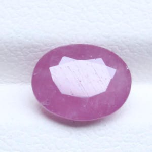 Peut inclure: Une pierre précieuse à facettes de forme ovale avec une teinte rose vive. La pierre présente une surface polie avec de multiples facettes géométriques qui reflètent la lumière, créant un aspect clair et brillant sur ses bords arrondis.