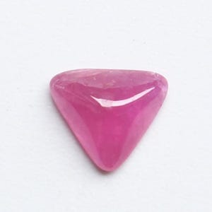 Pode incluir: Uma pedra preciosa triangular polida em um tom rosa vibrante. A gema tem uma superfície lisa e arredondada e uma qualidade translúcida, que capta a luz. A forma é um triângulo equilátero perfeito, ideal para joias ou coleção.