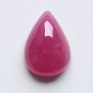 May include: A magenta-coloured, teardrop-shaped gemstone with a polished finish. The gem's surface is smooth and glossy, reflecting light. The stone is set against a plain white background, accentuating its colour and form. Suitable for jewellery making.