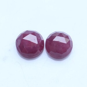 Può includere: Due gemme rotonde di rubino sfaccettato. I rubini sono di un colore rosso intenso e ricco e hanno un aspetto brillante e scintillante. Le gemme sono su uno sfondo bianco.