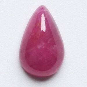 May include: A polished, teardrop-shaped gemstone in a vibrant magenta hue. The gem has a smooth, reflective surface, with subtle internal variations in colour. The overall shape is elongated, tapering to a rounded point.