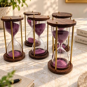 Peut inclure: Un ensemble de quatre sabliers dotés de bases et de sommets circulaires en bois foncé, reliés par de fines tiges en métal doré. Chaque récipient en verre transparent contient du sable violet vif, s'écoulant par le goulot central.