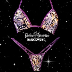 May include: A two-piece dancewear set featuring a purple and animal print design. The top is a triangle bikini style, and the bottom is a thong. The set is made of a shiny, metallic fabric. The text "Divine Feminine DANCEWEAR" is visible.