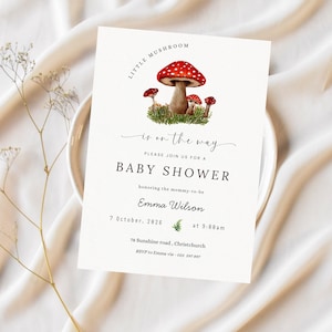 May include: A baby shower invitation with a watercolor illustration of red mushrooms with white spots. The text reads "Little Mushroom is on the way" and includes details for the event, such as the date, time, and location.