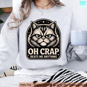 Könnte beinhalten: Ein hellgraues Sweatshirt mit einer Schwarz-Weiß-Illustration eines wütenden Katzengesichts. Der Text "OH CRAP BEATS ME ANYTHING" befindet sich unter dem Katzenbild. Das Sweatshirt ist ein digitaler Download.