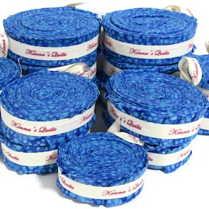 May include: Several rolls of blue patterned fabric, each with a white band printed with "Konna's Quilts" in red. The fabric has a speckled design. White ribbons are attached to the rolls. The rolls are stacked in a group.