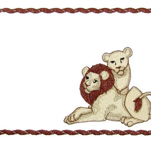 May include: A brown rope frame with a white background. Inside the frame is an embroidered image of a lion and a lion cub. The lion is lying down with its head turned to the side. The lion cub is sitting on top of the lion's back.