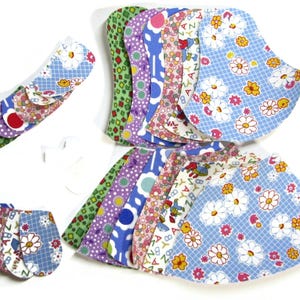 May include: A selection of reusable cloth menstrual pads in diverse floral and patterned designs. The pads display a variety of colours, including blue, green, purple, and pink, with daisy, polka dot, and letter prints. Several pads are stacked and fanned out.