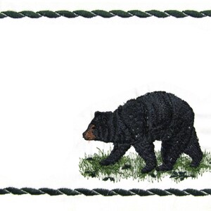 May include: An embroidered black bear on a white background with a green rope border.