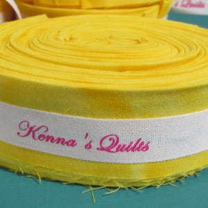 May include: A yellow fabric roll with a white label that says "Kenna's Quilts" in pink lettering.