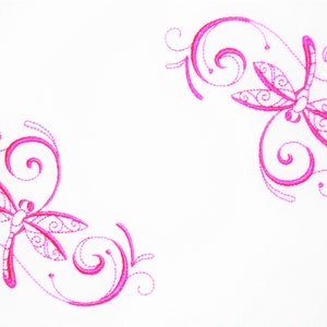 May include: White fabric featuring embroidered pink dragonflies and swirling floral patterns. The dragonflies, with detailed wings, are placed in opposite corners, forming a decorative design.