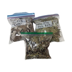 Op de afbeelding: Drie doorzichtige plastic zakken gevuld met gedroogde bladeren. Elke zak is afgesloten met een ritssluiting. De zakken hebben handgeschreven labels met de tekst "Ziploc Fey Trumpet", "Ziploc Fey Bula Kaka" en "Manga".
