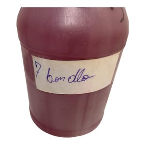 May include: A cylindrical, burgundy-colored container with a white label. The label has the number "7" and the handwritten words "bon dlo" in blue ink. The container is made of a smooth, opaque material.