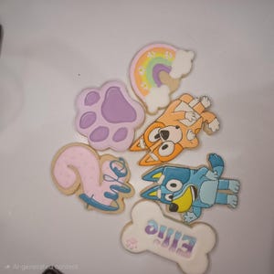 Op de afbeelding: Assortiment van versierde koekjes met stripfiguren, een pootafdruk, een regenboog en een botvormig koekje met de naam "Ellie". De koekjes zijn versierd met pastelkleuren en glazuur.
