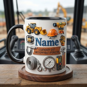 May include: White ceramic mug with a black handle and rim, decorated with construction equipment illustrations. Includes a yellow digger, orange hard hat, and the text "Name" above "Legendary Dad, Unstoppable Operator."