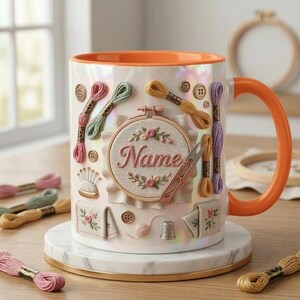 Puede incluir: Una taza de cer&aacute;mica blanca con asa e interior naranja, decorada con adornos de tem&aacute;tica de bordado. El dise&ntilde;o incluye carretes de hilo, botones, tijeras y un bastidor de bordado con el nombre "Name".