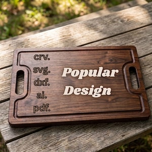 May include: A rectangular dark brown wooden cutting board with two side handles and a juice groove. The board features the engraved text "crv.", "svg.", "dxf.", "ai.", and "pdf." on the left side, with the words "Popular Design" in the center.