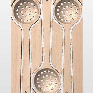 May include: A light-colored wooden board featuring three laser-cut slotted spoons. Two spoons are positioned vertically at the top, while the third spoon is centered below them, all integrated into the flat wooden surface with visible cutouts.