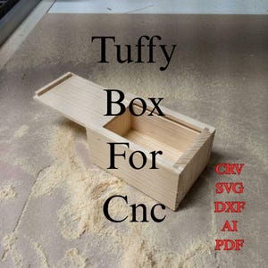 Puede incluir: Una caja de madera de color claro con tapa deslizante, que presenta el texto Tuffy Box For Cnc y los formatos de archivo CRV, SVG, DXF, AI y PDF. La caja tiene una forma rectangular con veta de madera visible y un compartimento interior.