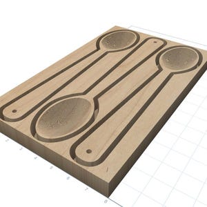 May include: A light brown wooden spoon mold with three spoon-shaped indentations. Each indentation has a detailed spoon bowl design and a small hole at the end of the handle. The mold is rectangular and has a natural wood grain.
