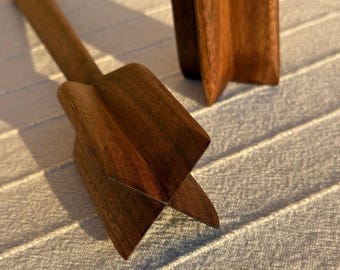 Peut inclure: Un presse-agrume en bois brun foncé doté d'un long manche fin et d'une tête en forme d'étoile à quatre branches aux bords tranchants et anguleux. L'outil est fabriqué à partir d'une seule pièce de bois avec un grain visible et une finition lisse.
