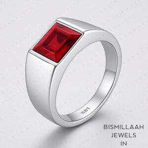 Puede incluir: Un anillo plateado con una gema rectangular de color rojo intenso. El anillo tiene una banda lisa y pulida y un engaste de bisel. Un dise&ntilde;o cl&aacute;sico, adecuado para el uso diario.