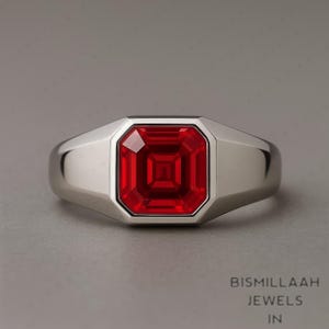 Puede incluir: Un anillo de plata con una gran gema roja vibrante de corte cuadrado. La gema está engastada en un bisel y la banda es de plata pulida. Una pieza llamativa, ideal para añadir un toque de color.