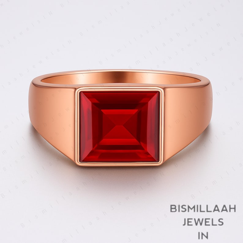 Puede incluir: Un anillo de oro rosa con una gran gema roja brillante de forma cuadrada. El anillo tiene una banda lisa y pulida y un dise&ntilde;o moderno y minimalista. La gema est&aacute; empotrada.