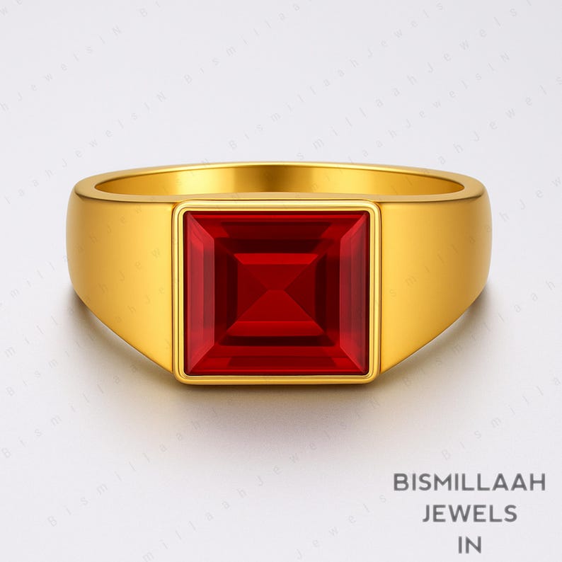 Puede incluir: Un anillo dorado con una gema roja intensa de forma cuadrada en el centro. El anillo tiene una banda gruesa y un acabado pulido. Joyas de Bismillaah Jewels.