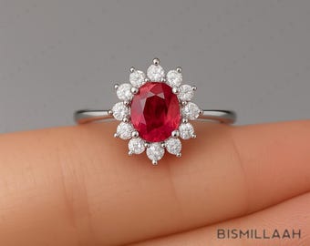 May include: A silver ring with an oval ruby centre stone, encircled by a halo of small, round, white diamonds. The ring's design is classic and elegant, highlighting the ruby's vibrant red colour and the diamonds' sparkle. A beautiful piece of jewellery.