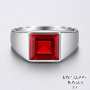 Puede incluir: Un anillo plateado con una gran gema roja brillante de forma cuadrada en el centro. El anillo tiene una banda lisa y pulida y un diseño moderno. La gema está engastada en un bisel cuadrado.
