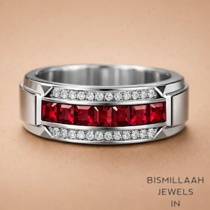 Peut inclure: Une bague en argent au design rectangulaire. La bague présente une rangée de pierres précieuses carrées rouge foncé au centre, bordée de deux rangées de petites pierres précieuses claires. La bague a une finition polie et est posée sur un fond neutre.
