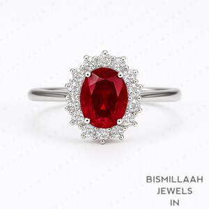 May include: A silver ring featuring a large, oval-cut ruby gemstone surrounded by a halo of smaller, round diamonds. The ruby is a deep red color, and the diamonds sparkle against the white background. The ring is a classic design.