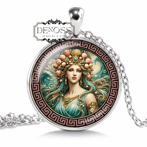 May include: A silver-toned circular pendant necklace featuring a central illustration of a figure with flowing teal hair, a seashell crown, and turquoise jewellery. The border displays a black and pink Greek key pattern. The text DENOSS JEWELRY & GIFT is visible.