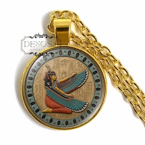 May include: A gold-toned pendant necklace featuring a circular frame with a glass-covered insert. The insert displays an Egyptian-style figure with outstretched wings, surrounded by hieroglyphs. The text DENOSS JEWELRY is visible.