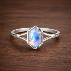 Può includere: Un anello d'argento con una pietra preziosa esagonale, azzurra e bianca. La fascia dell'anello si divide in un design a doppia fascia su ciascun lato della pietra preziosa, creando un aspetto aperto e arioso. La pietra preziosa è incastonata in una lunetta d'argento.