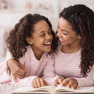Pu&ograve; includere: Una madre e una bambina ridono mentre leggono un libro insieme. La bambina indossa una camicia rosa chiaro a maniche lunghe, e la madre indossa una camicia a righe rosa e bianca a maniche lunghe. Il libro &egrave; aperto e lo guardano entrambe.