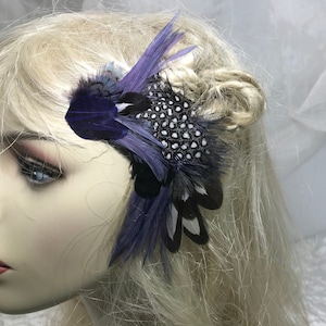 Könnte beinhalten: Eine Haarklammer aus lila und schwarzen Federn mit weißen Punkten. Die Klammer besteht aus Federn und ist an einer Metallklammer befestigt.