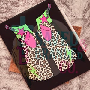 May include: A black, glossy surface features a colorful illustration of two cowboy boots. The boots have a leopard print design, pink heels, and green tops with pink star accents. A white stylus rests on the right side.