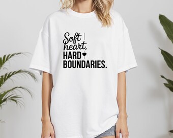 May include: White t-shirt featuring the text "Soft heart, HARD BOUNDARIES." in black script. The shirt has a relaxed fit and short sleeves. The word "WHITE" is in the upper left corner.